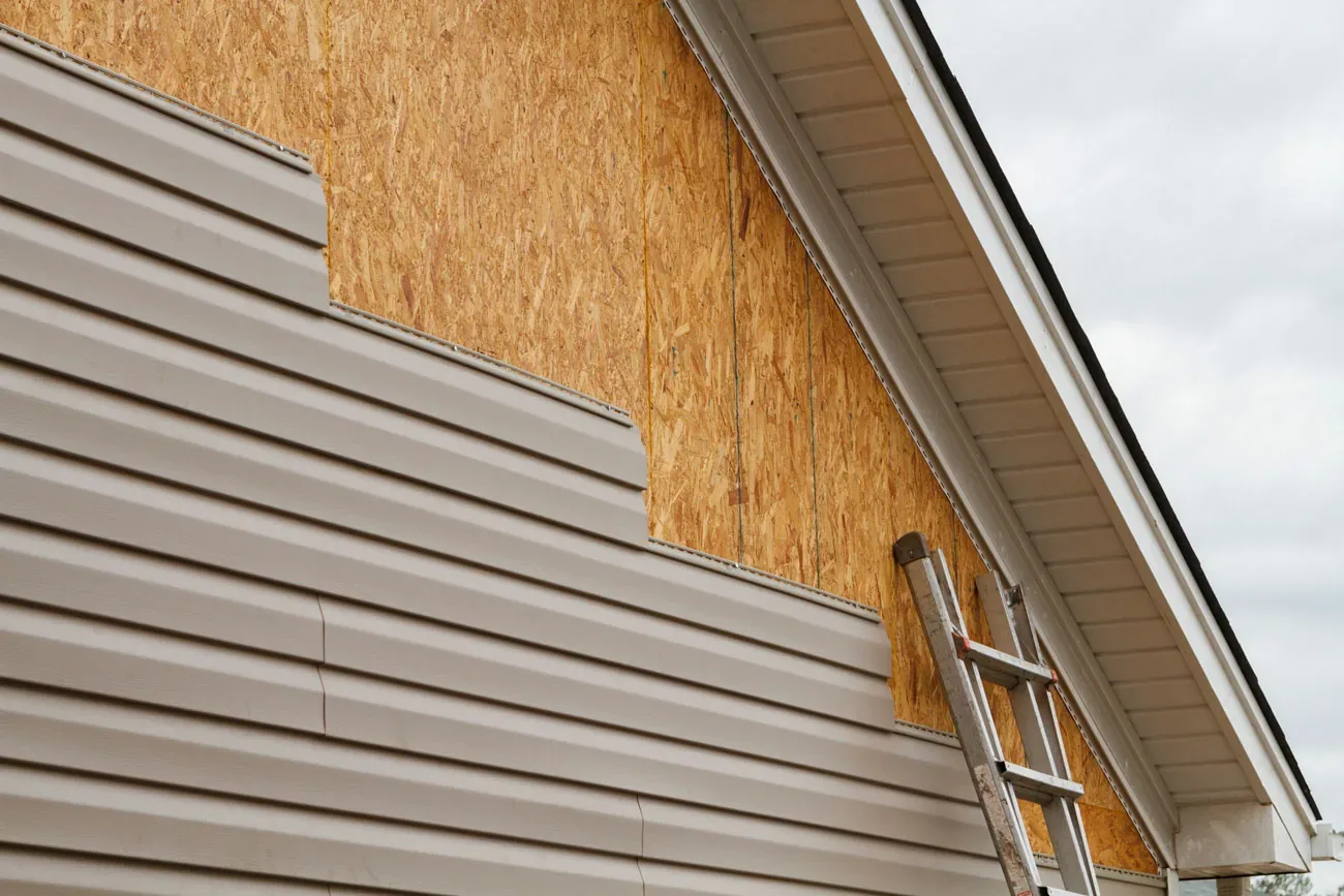 New siding being installed over sheathing with a ladder