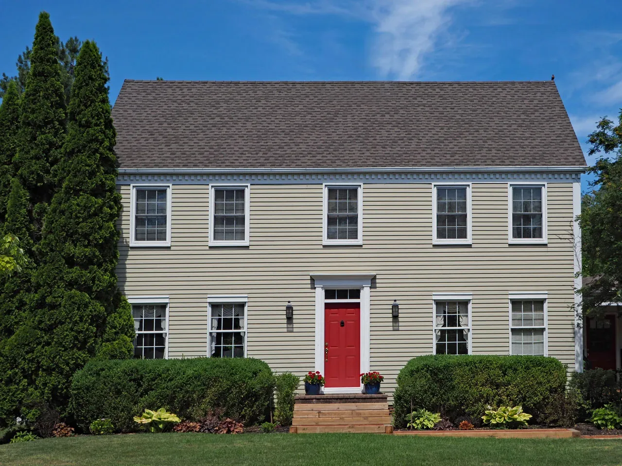 Colonial home with new white double-hung windows and a red front door